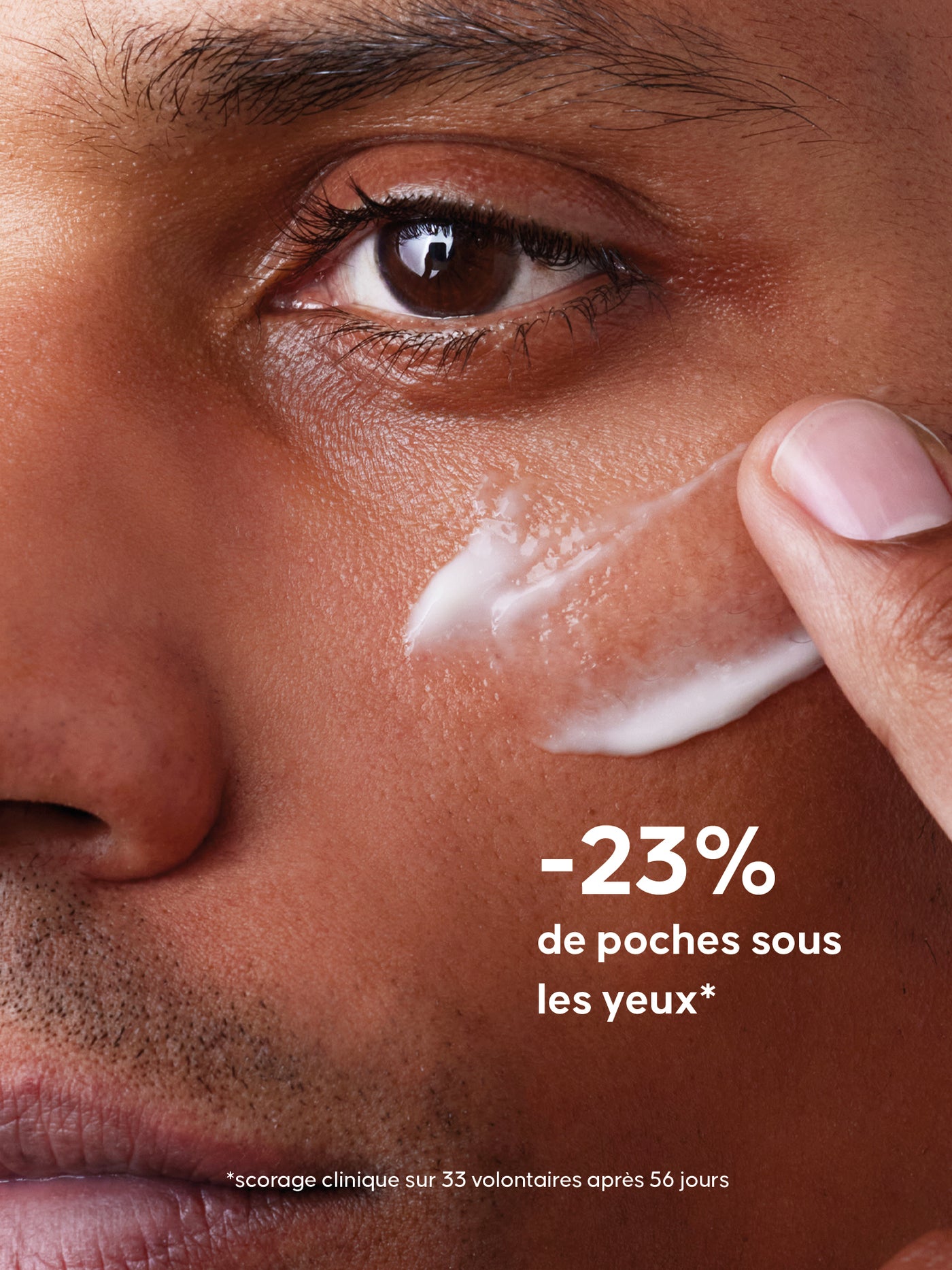 Gros plan d’un homme appliquant La Crème Fluide sous son œil avec le bout du doigt et la mention "-23% de poches sous les yeux"