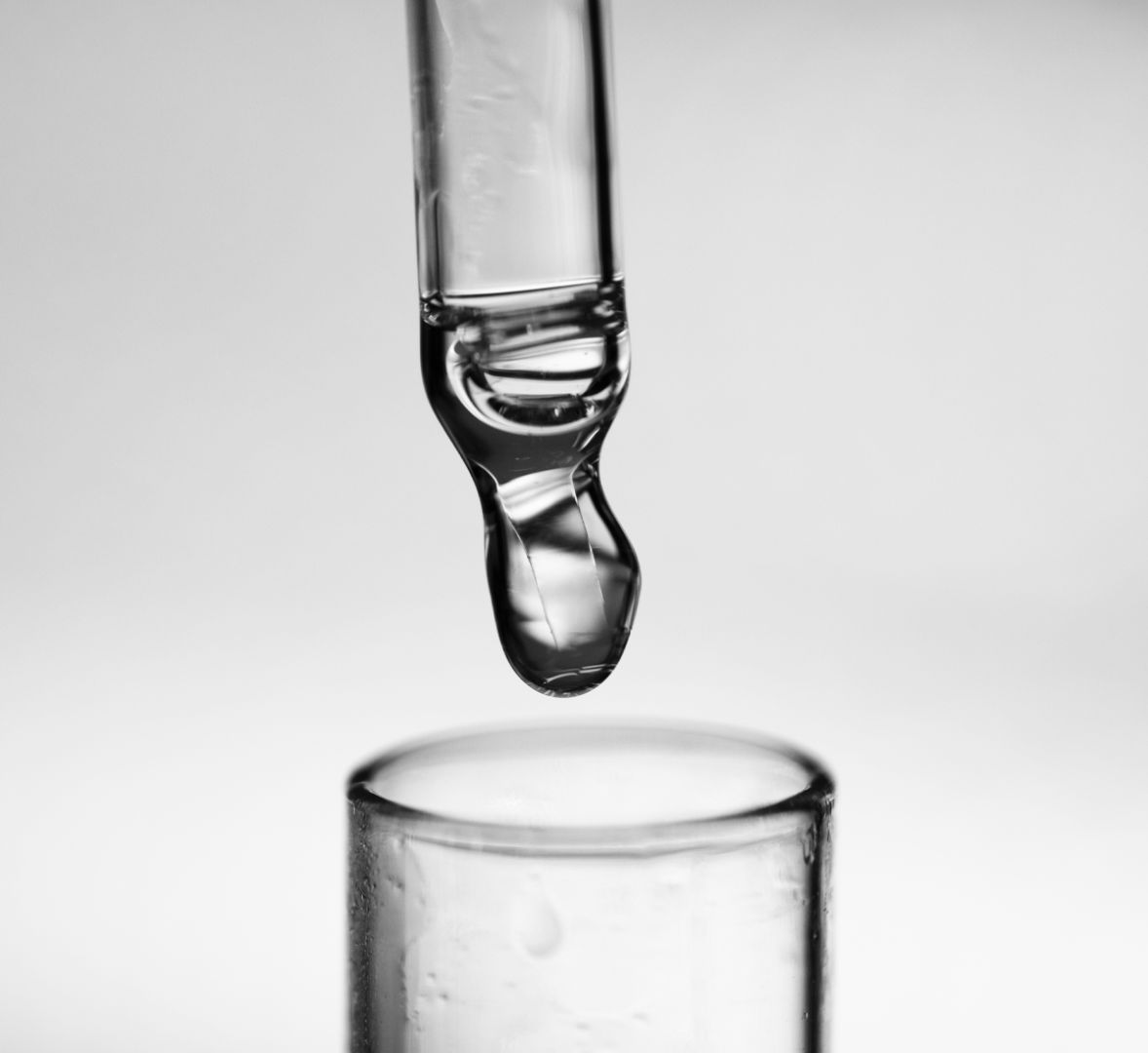 Pipette en verre libérant une goutte de niacinamide au-dessus d’un tube en verre, photographiée en noir et blanc