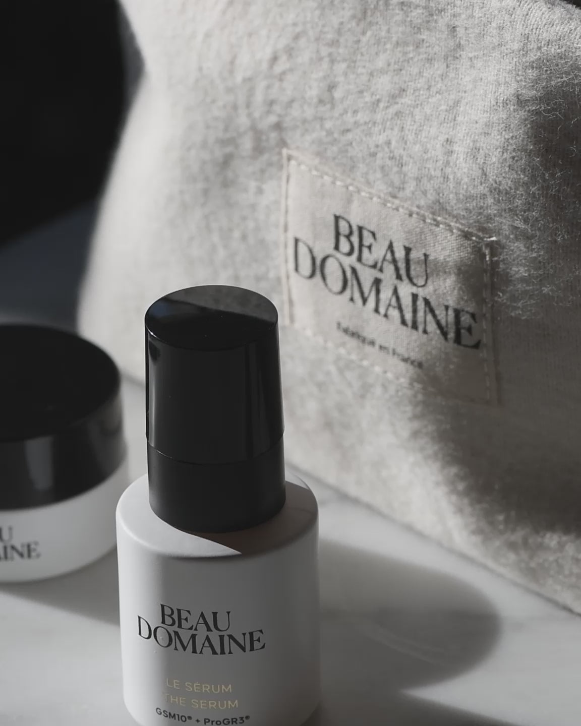 Gros plan des produits de La Routine Découverte, avec un flou artistique, et une pochette avec l'inscription Beau Domaine et une main qui prends un produit d'au dessus